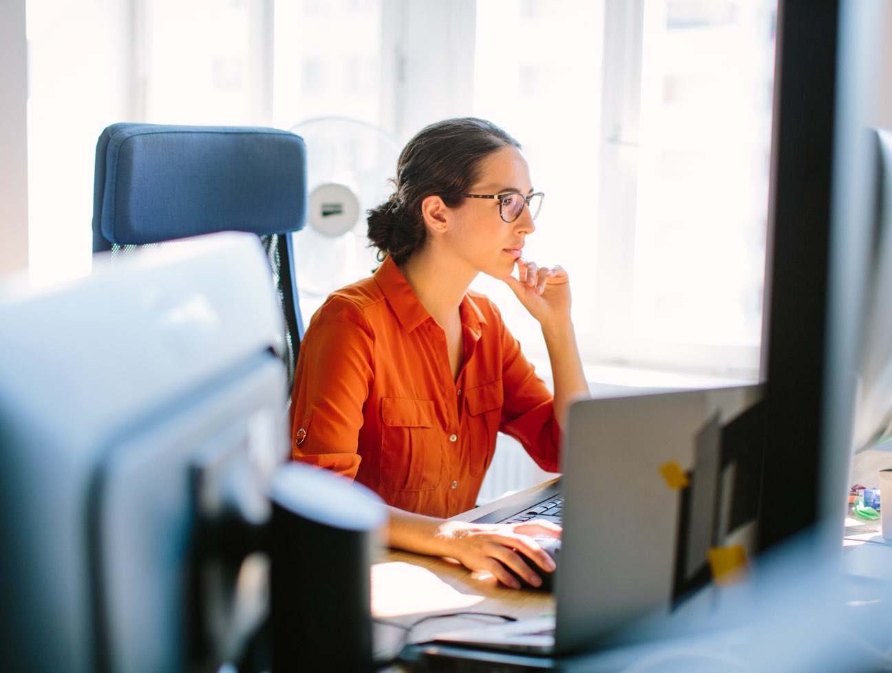 Woman wearing orange shirt and glasses staring off into her computer