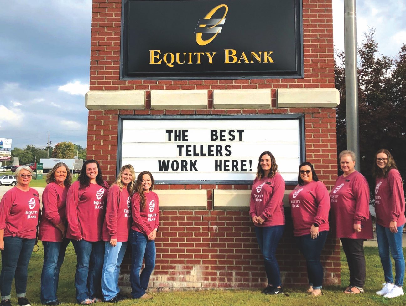 A group of Equity Bank employees flanking an exterior bank sign.